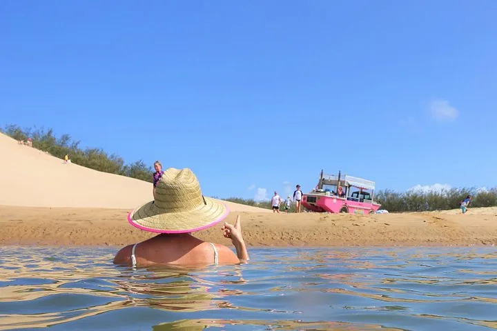 Eine Frau mit Strohhut beim Schwimmen im Wasser nahe einem Sandstrand