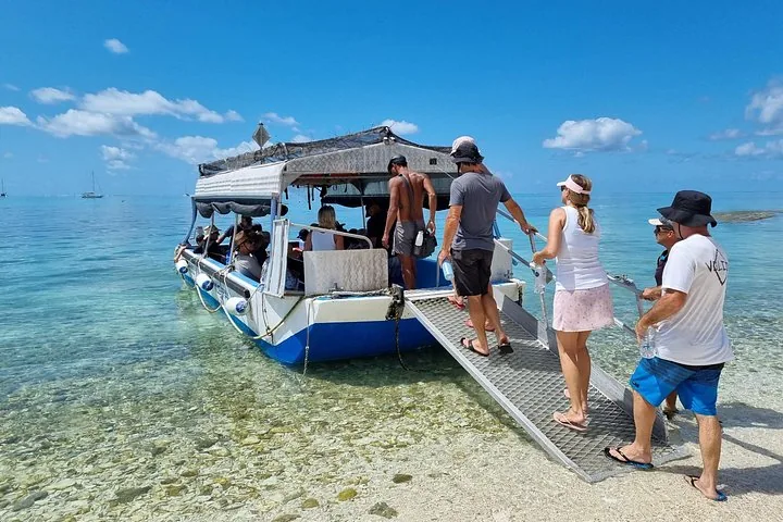 Touristen besteigen vom Sandstrand aus ein Glasbodenboot für die Fahrt aufs Meer